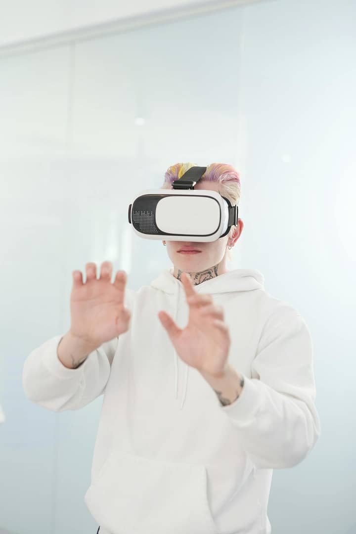 Tattooed person with colored hair immersed in virtual reality using a headset indoors.